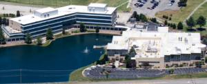 Large two building campus off I-40 interstate separated by lake with a fountain Apex Bank Has Purchased New Campus for its Headquarters